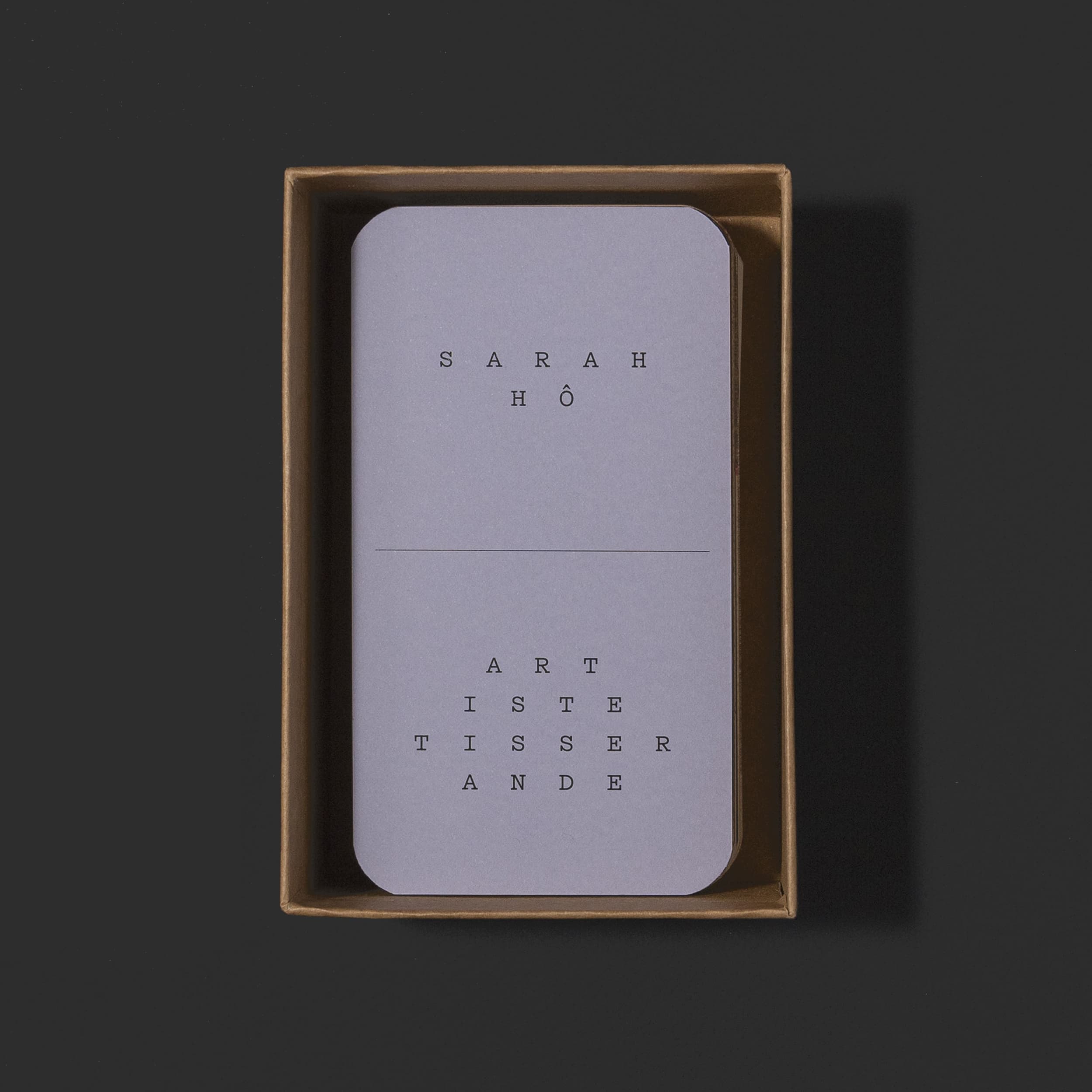 Boîte ouverte avec une carte d'introduction violette, on peut y lire "Sarah Hô, artiste tisserande"
